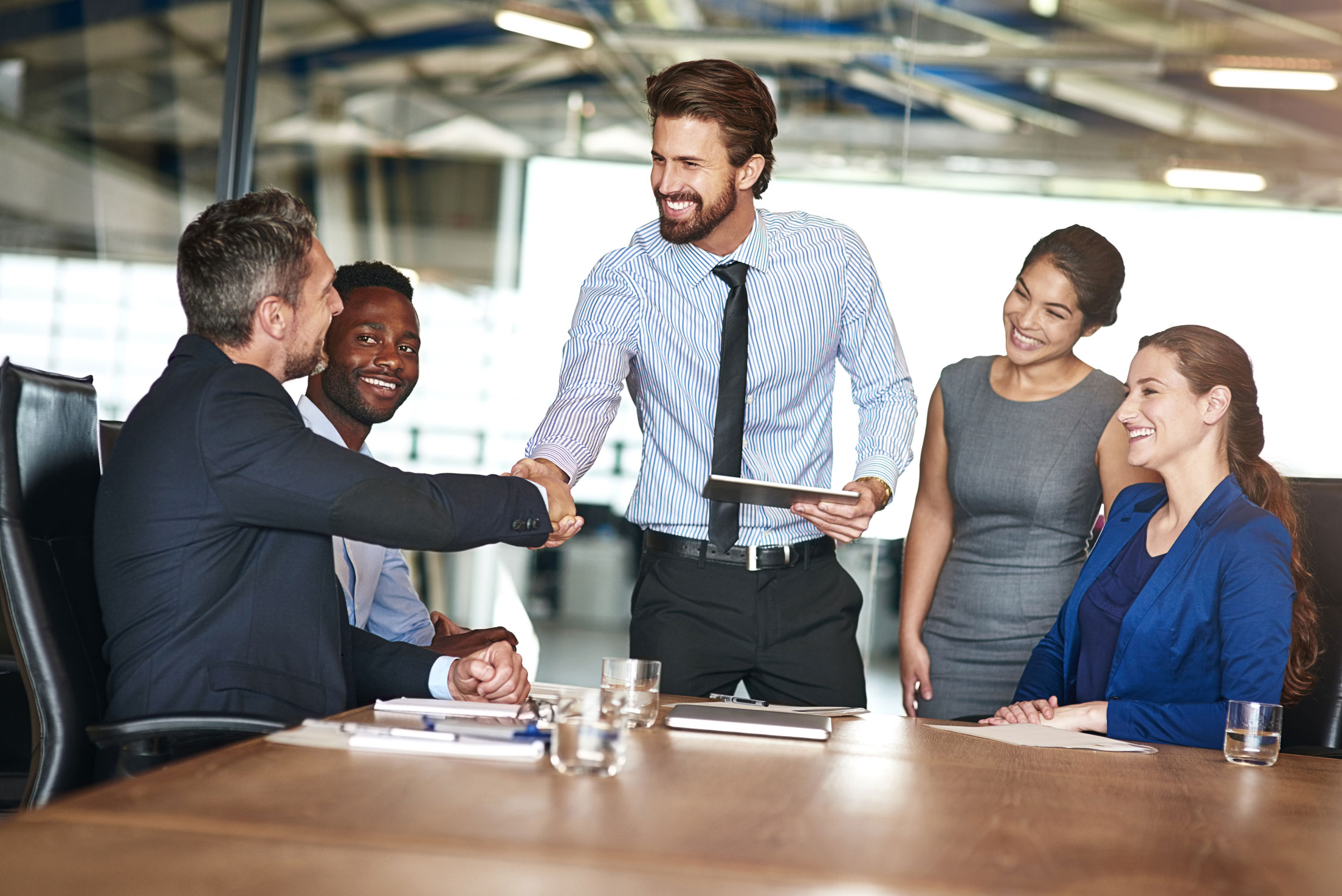 Two colleagues shaking hands while in a meeting with colleagues in a boardroom